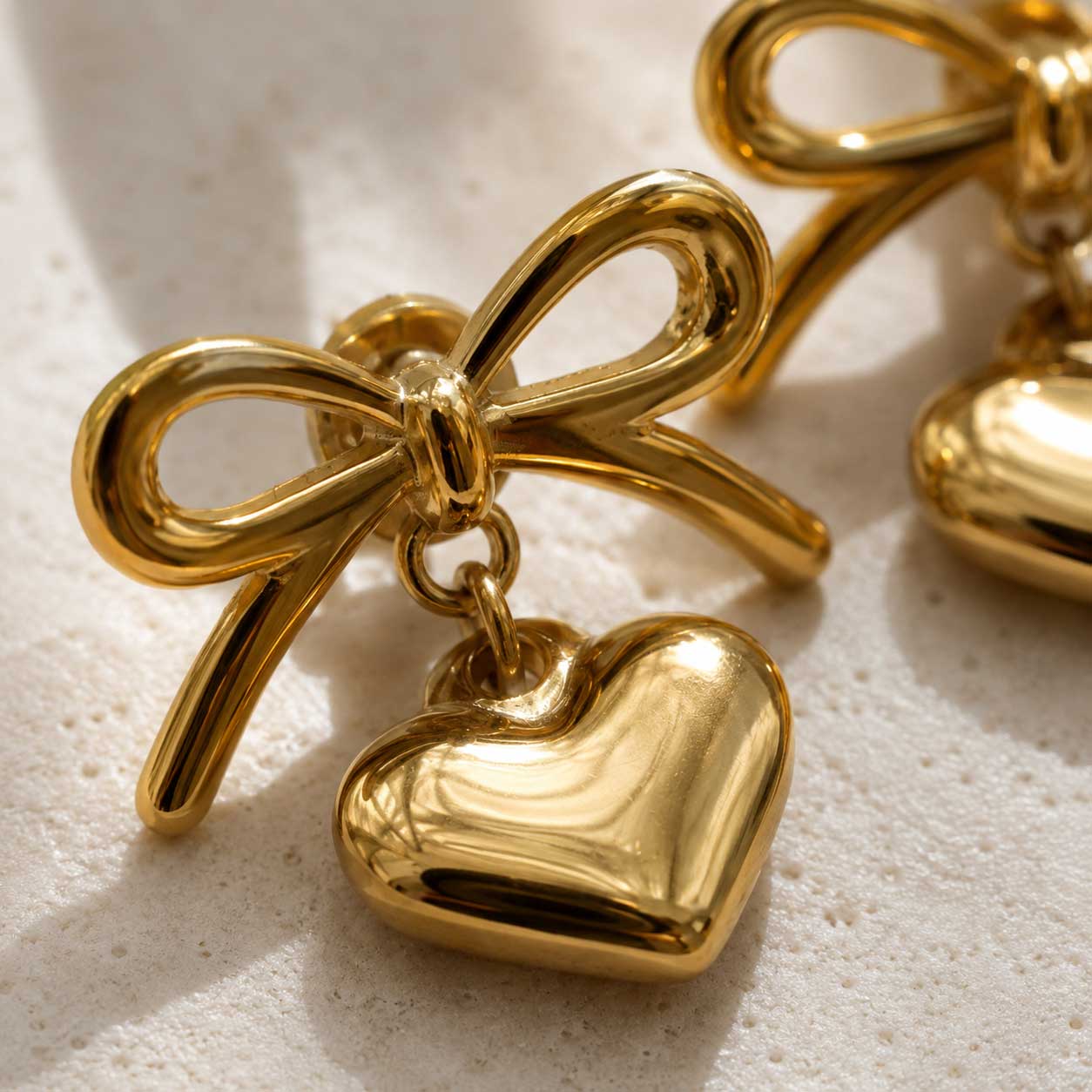 Nahaufnahme goldener Schleifenohrringe mit Herzanhänger aus Edelstahl – Detail des Steckverschlusses – Saltyblush
