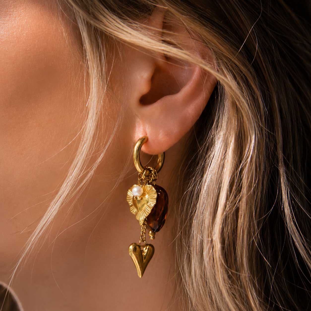Frau trägt goldene Creolen heartbeat mit Herz-Charm und brauner Perle am Ohr – Nahaufnahme Lifestyle | Saltyblush