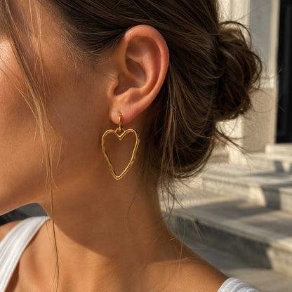 Frau mit braunem Dutt trägt die Heartline goldenen Herz-Ohrringe aus Edelstahl im Sonnenlicht – Saltyblush
