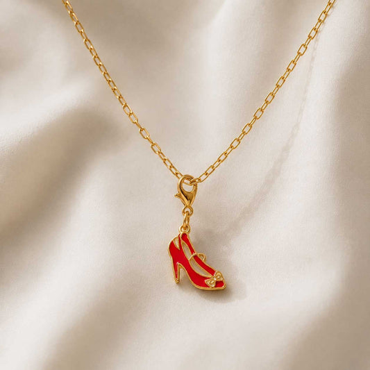Goldene Gliederkette mit rotem High Heel Charm hängend auf cremefarbenem Seidenstoff – Saltyblush
