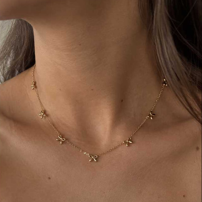 Goldene Halskette aus Edelstahl mit Schleifenanhänger am Hals getragen, zarter Schmuck für feminine Alltagslooks und elegante Layering-Kombinationen
[AI]