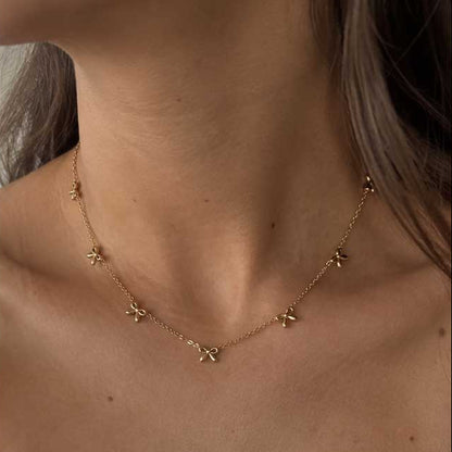 Goldene Halskette aus Edelstahl mit Schleifenanhänger am Hals getragen, zarter Schmuck für feminine Alltagslooks und elegante Layering-Kombinationen
[AI]