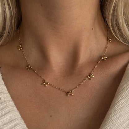 Goldene Halskette aus Edelstahl mit Schleifenanhänger am Hals getragen, zarter Schmuck für feminine Alltagslooks und elegante Layering-Kombinationen
