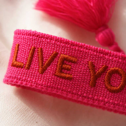 Nahaufnahme der roten Stickerei Live Your Dreams auf pinkfarbenem Textilarmband – Saltyblush
