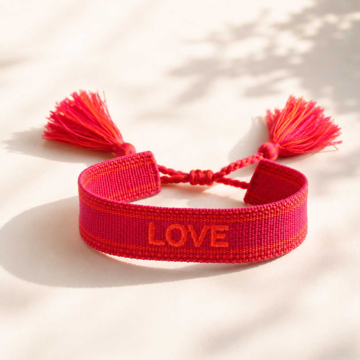 Rotes gewebtes LOVE Armband mit Quasten auf hellem Untergrund, verstellbares Stoffarmband mit besticktem Schriftzug
