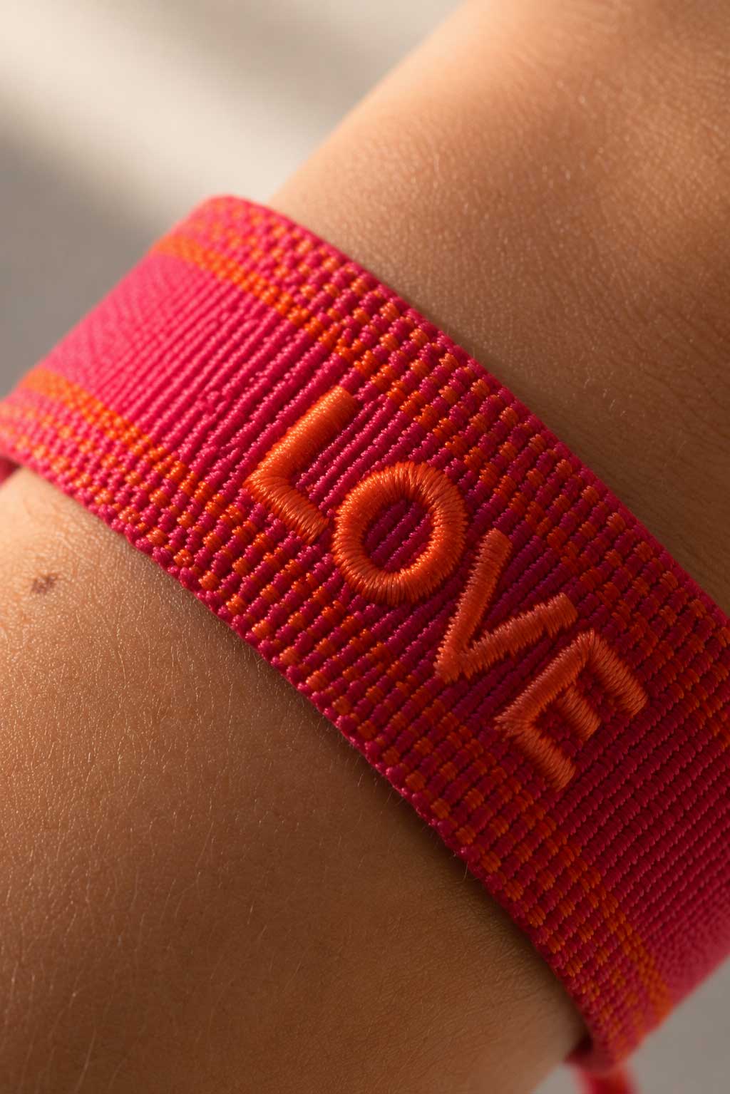 Nahaufnahme des bestickten LOVE-Schriftzugs auf rotem gewebtem Armband, Detailansicht der orangefarbenen Stickerei auf Webstoff
