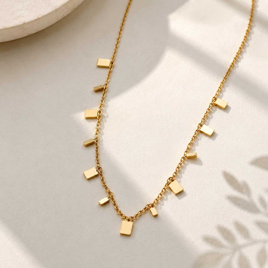 Goldene Halskette mit rechteckigen Plättchen – Minimalist Chic Halskette von Saltyblush, filigrane Goldkette mit 11 kleinen Rechteck-Charms, Flatlay auf hellem Hintergrund
