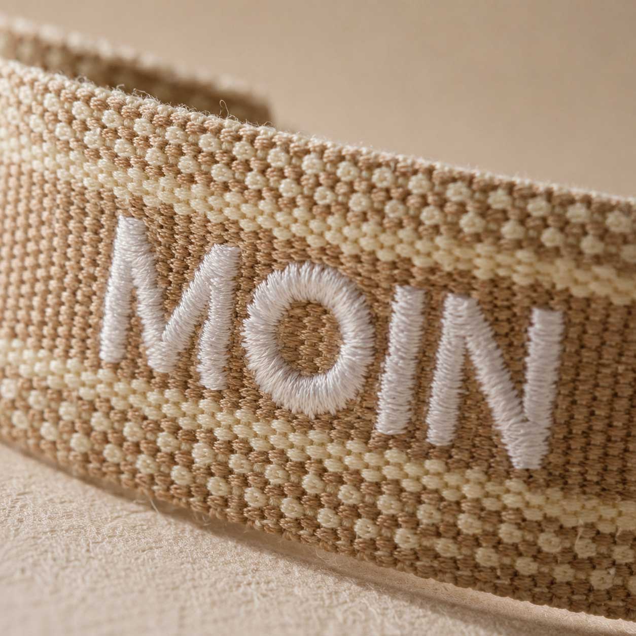 Nahaufnahme der weißen MOIN Stickerei auf beige-cremefarbenem gewebtem Textilarmband – Saltyblush
