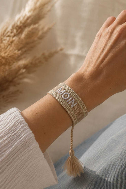 Beiges MOIN Armband mit cremefarbener Quaste am Handgelenk getragen, weißes Oberteil, Pampasgras im Hintergrund – Saltyblush

