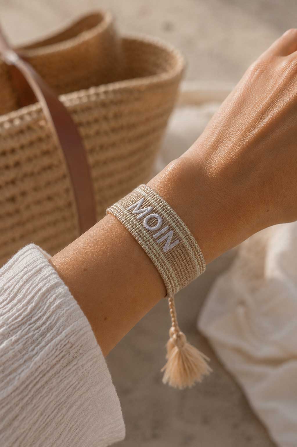 Beiges MOIN Statement Armband am Handgelenk getragen, weißes Oberteil, Korbhandtasche im Hintergrund – Saltyblush
