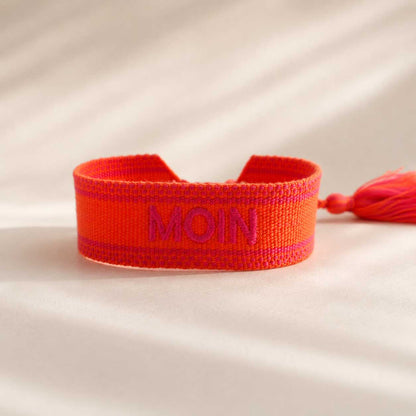 Oranges Statement Armband mit pinker MOIN Stickerei und roter Quaste, seitliche Ansicht auf hellem Untergrund – Saltyblush
