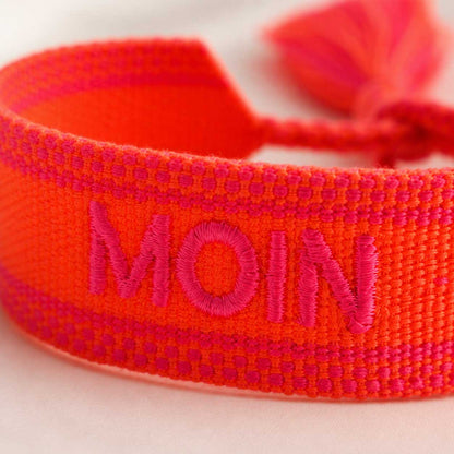 Nahaufnahme der pinken MOIN Stickerei auf orangem gewebtem Textilarmband – Saltyblush
