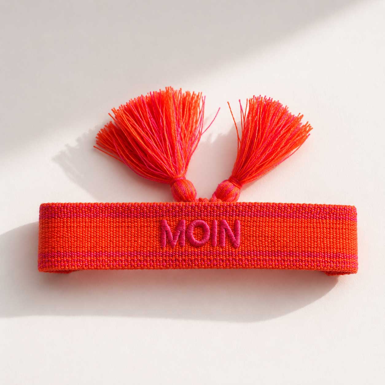 Oranges MOIN Statement Armband mit zwei orangeroten Quasten aufgeklappt, Draufsicht auf hellem Untergrund – Saltyblush
