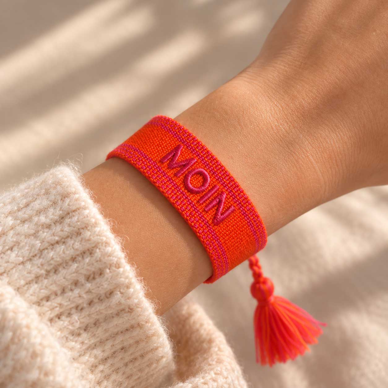 Oranges MOIN Armband mit roter Quaste am Handgelenk getragen, cremefarbener Strickpullover, Sonnenlicht – Saltyblush
