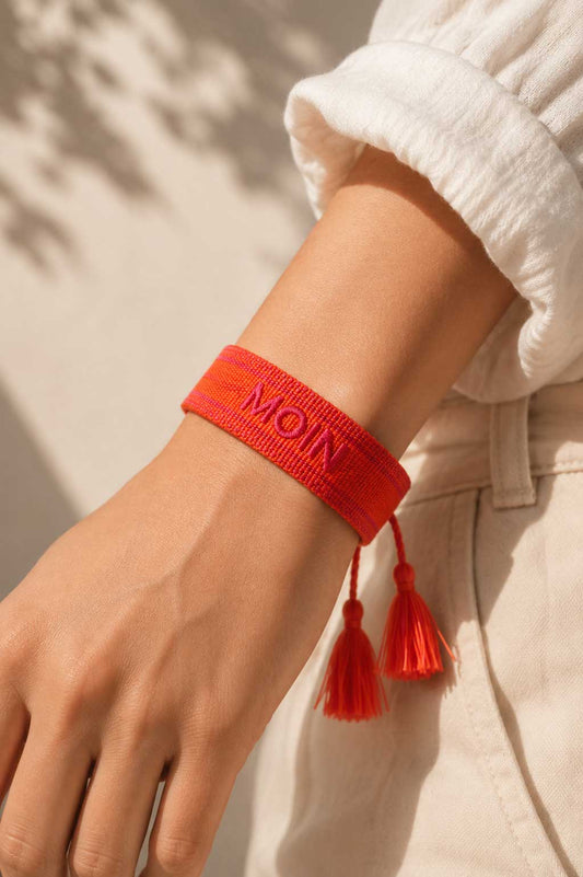 Oranges MOIN Armband mit zwei roten Quasten am Handgelenk getragen, weißes Leinenoberteil, sandiger Hintergrund – Saltyblush
