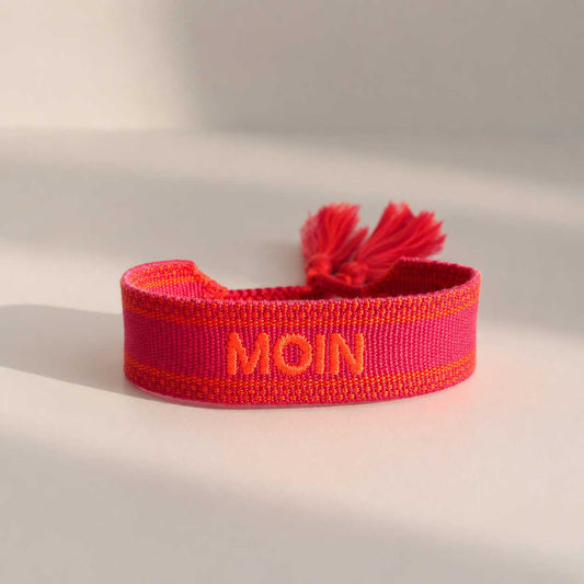 Pinkes Statement Armband mit oranger MOIN Stickerei und roten Quasten, seitliche Ansicht auf hellem Untergrund – Saltyblush
