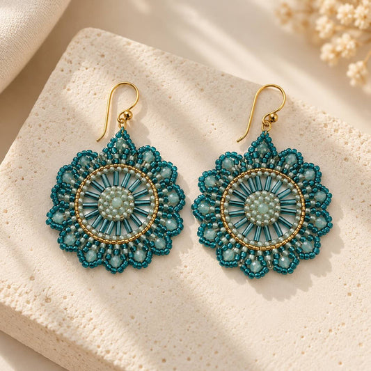 Ocean Mandala goldene Perlenohrringe – handgefertigtes Paar, rundes Mandala-Design aus türkisfarbenen Rocailles, weißen Glasperlen und türkisfarbenen Stäbchenperlen in goldenem Metallring, goldener Hakenverschluss, auf Travertin-Stein mit Schleierkraut 