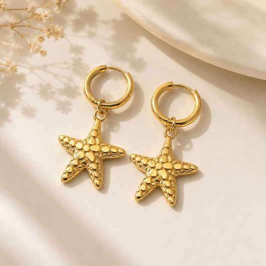 Ocean Star goldene Creolen mit Seestern-Anhänger auf cremefarbenem Hintergrund
