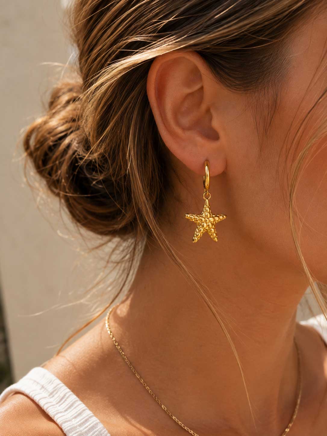 Frau trägt goldene Creolen mit Seestern-Anhänger ocean star am Ohr – Seitenansicht
