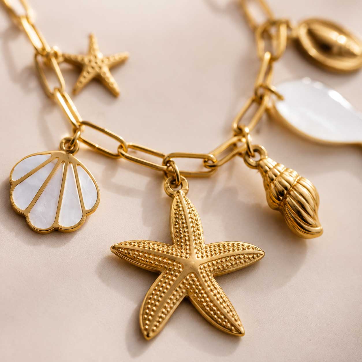 Nahaufnahme der Ocean Treasures Halskette – Detailansicht goldener Seestern, Perlmutt-Muschelschale, Schnecken-Charm und Perlmutt-Fisch auf vergoldeter Paperclip-Kette
