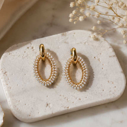 Pearl Glow Hoops – ovale Goldcreolen mit weißen Perlen auf hellem Hintergrund
