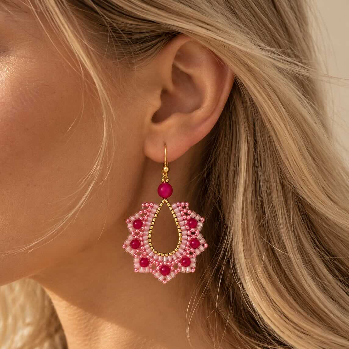 Pink Petal goldene Perlenohrringe getragen – blonde Frau, Nahaufnahme Ohr, großer rosa Boho-Tropfenanhänger mit pinken Perlenblüten und goldenem Hakenverschluss, warmes Sommerlicht 
[AI]