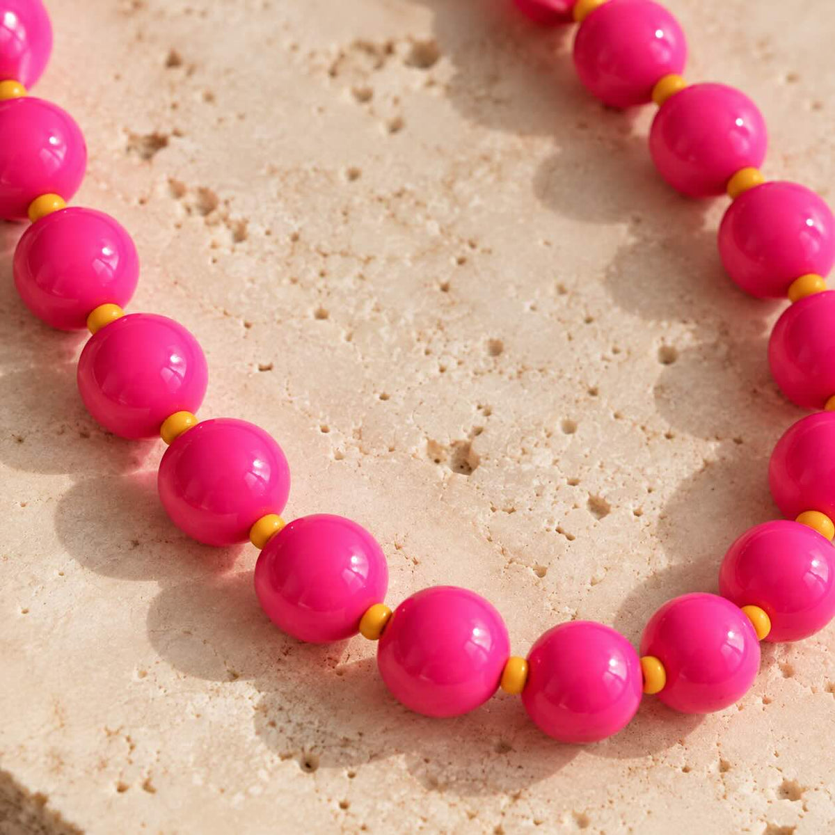 Nahaufnahme der glänzenden pinkfarbenen Perlen und kleinen orangefarbenen Zwischenperlen des Phone Charms auf hellem Stein.
