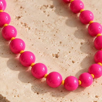 Nahaufnahme der glänzenden pinkfarbenen Perlen und kleinen orangefarbenen Zwischenperlen des Phone Charms auf hellem Stein.
