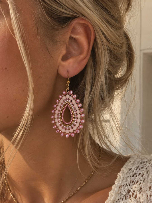 Rosewater goldene Perlenohrringe getragen – blonde Frau, Nahaufnahme Ohr, rosa Boho-Tropfenohrringe mit goldenem Hakenverschluss, heller Hintergrund
