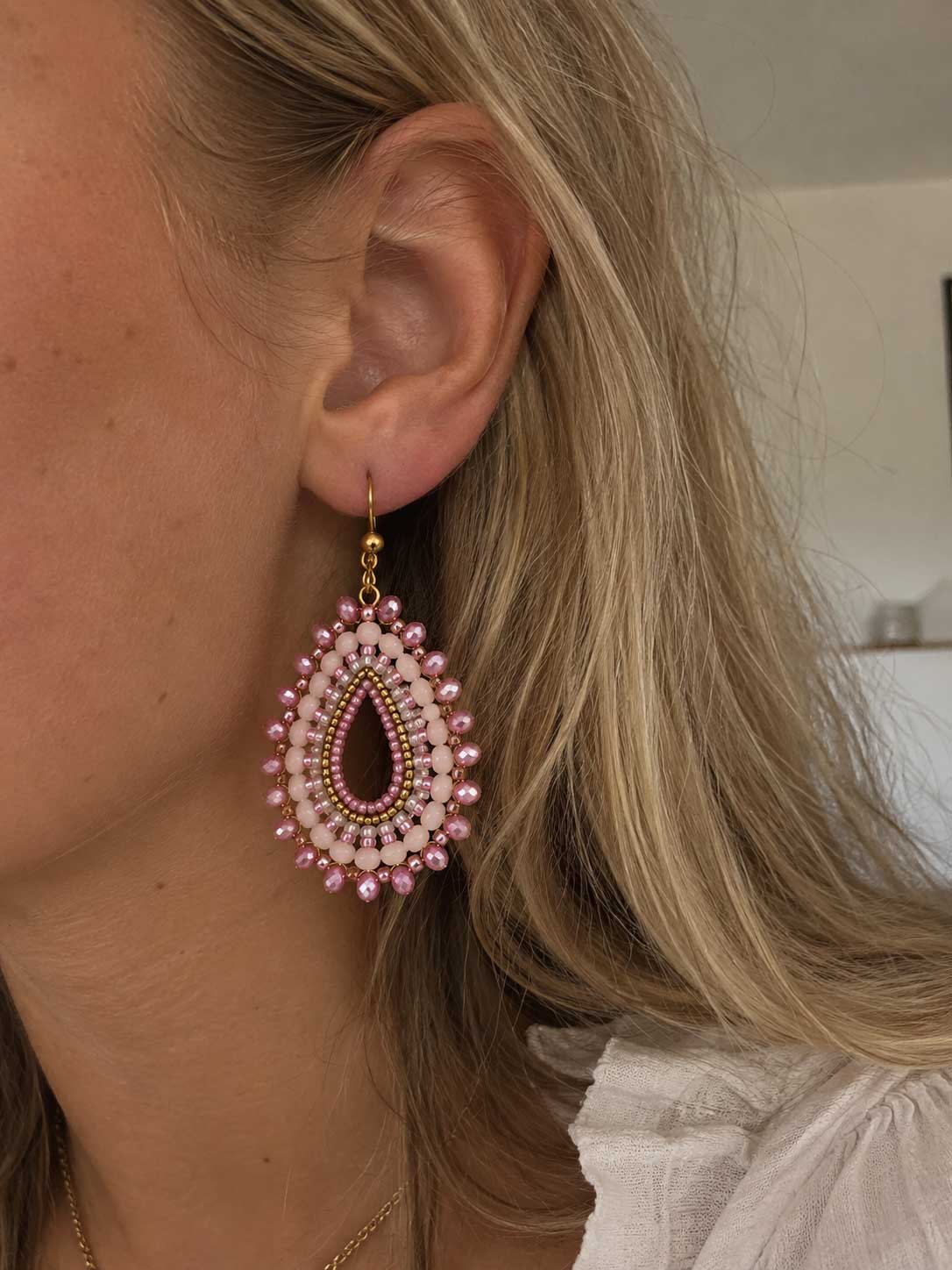 Rosewater goldene Perlenohrringe getragen – blonde Frau, Seitenansicht, großer rosa Boho-Tropfenanhänger mit goldenen Perlen, weißer Hintergrund
