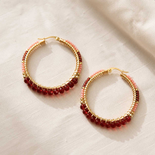 Goldene Creolen mit dunkelroten und hellrosa Kristallperlen auf weißem Leinenstoff, runde Perlen-Ohrringe mit Bordeaux-Rosa-Farbverlauf und goldenem Klappverschluss
