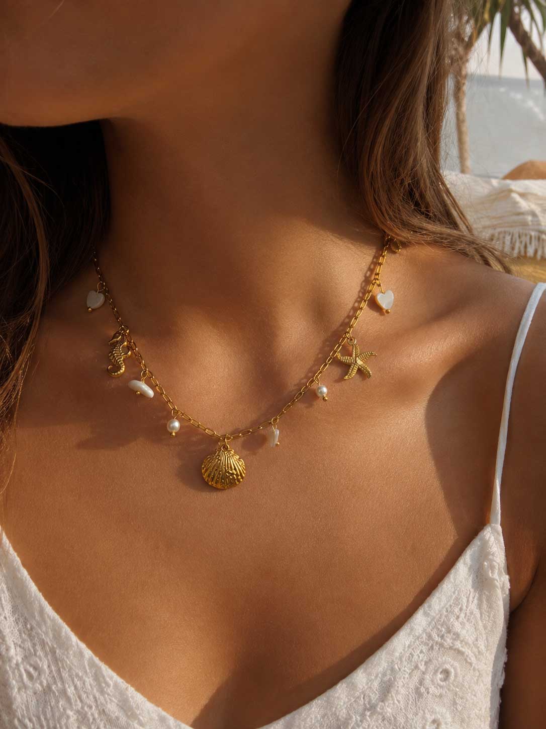 Salt Breeze Halskette Lifestyle – goldene maritime Halskette von Saltyblush am Hals einer Frau, sommerlicher Strandlook zu weißem Top, Muschel- und Perlenanhänger im Sonnenlicht
