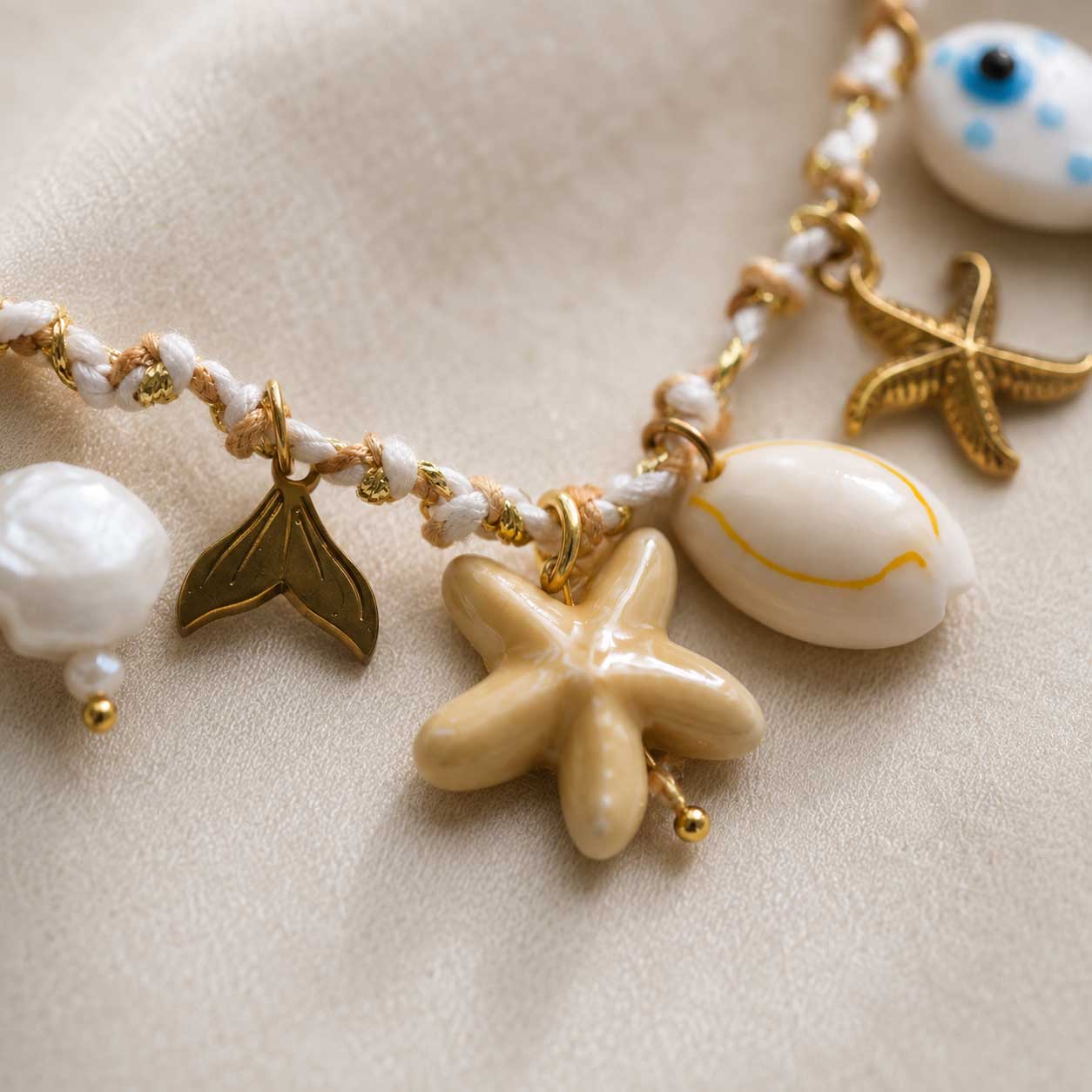 Nahaufnahme maritime Charms – Salty Star Halskette von Saltyblush, Seestern, Muschel, Meerjungfrauenflosse, Perle und Evil Eye Fisch an geflochtener Goldkette, Detailansicht
