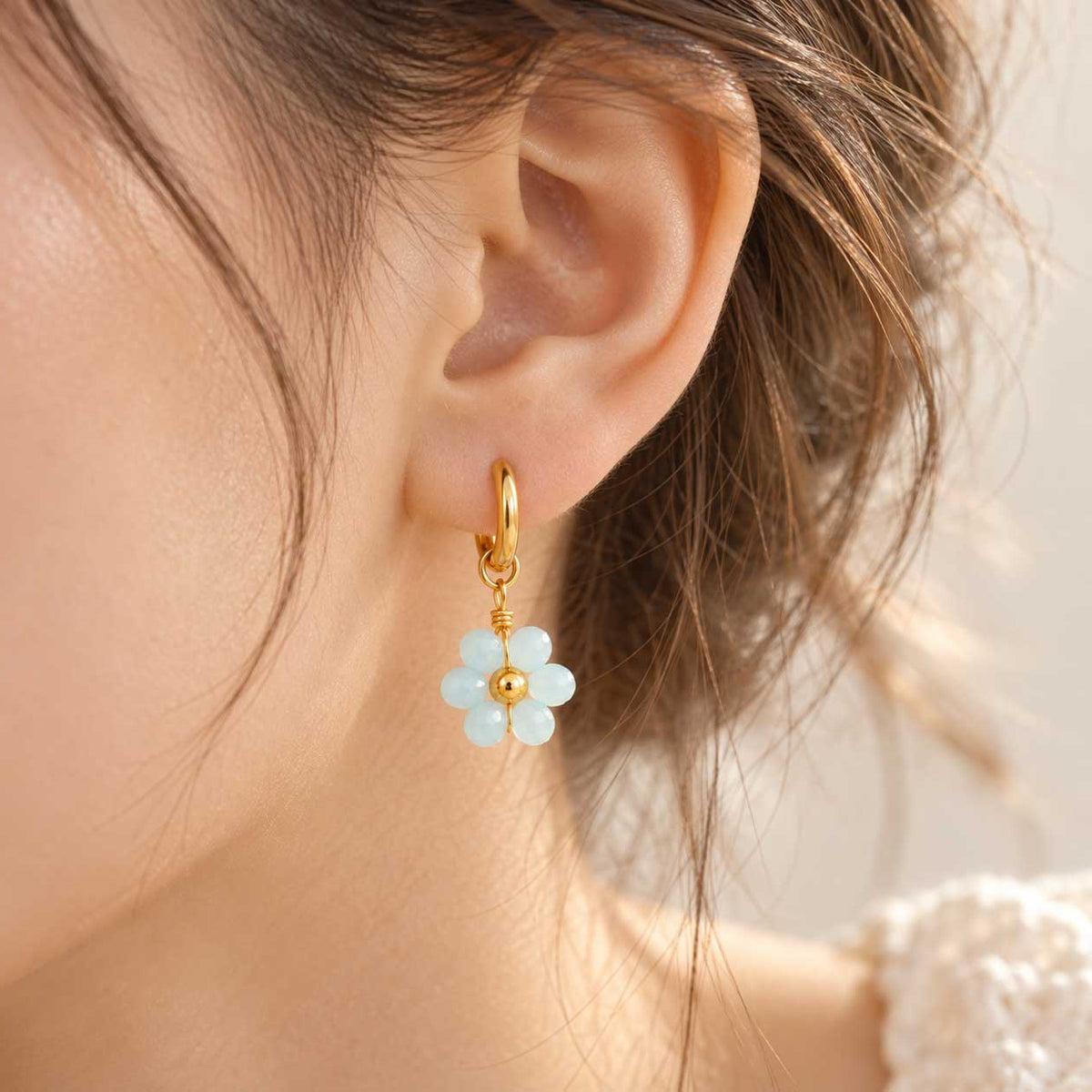Sea Blossom goldene Ohrringe getragen – brünette Frau, Seitenansicht, hellblauer Blütenanhänger mit goldenem Mittelpunkt, warmes Licht
[AI]