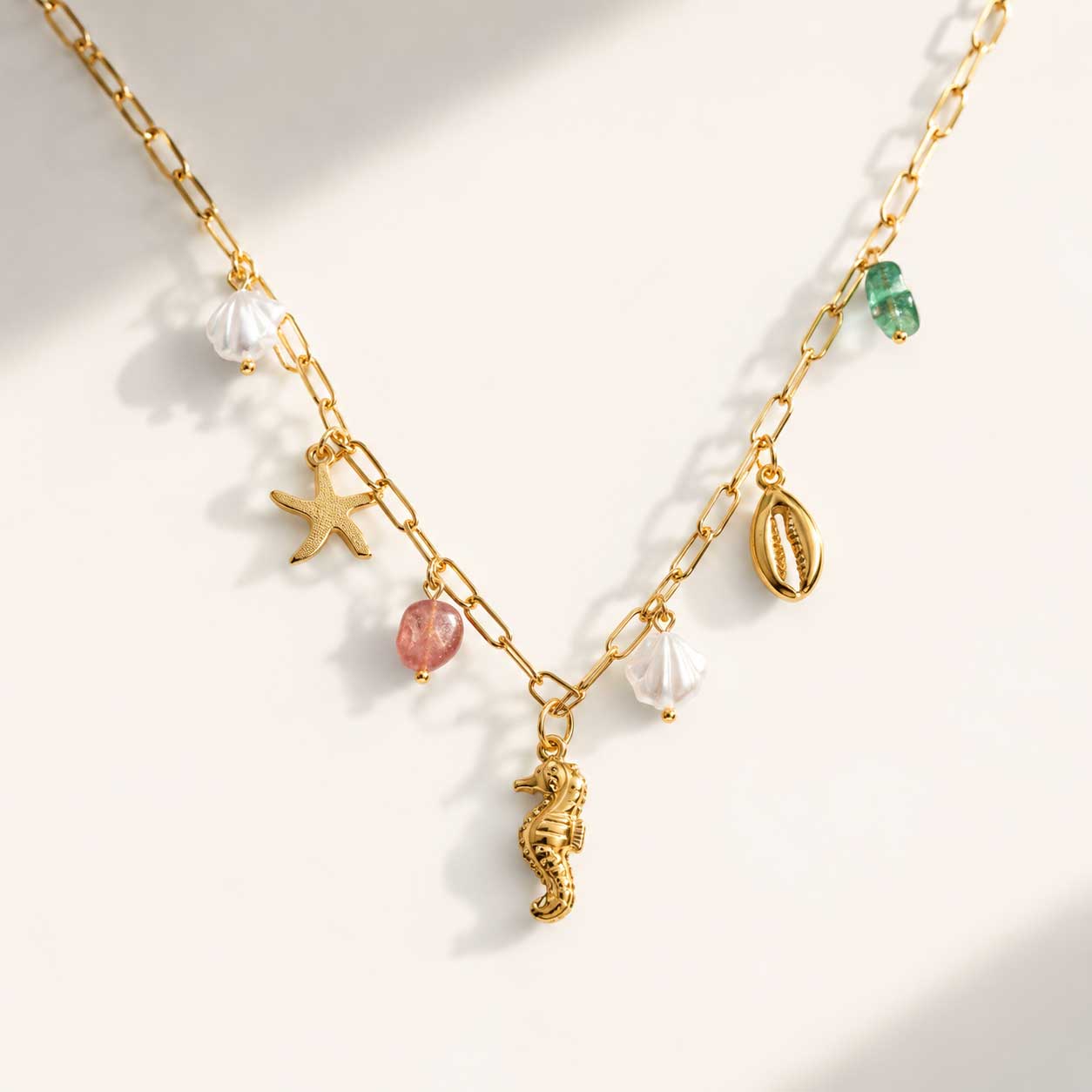 Sea Kiss goldene Halskette mit Seepferdchen, Seestern, Muschel und Perlen-Charms auf cremefarbenem Hintergrund
