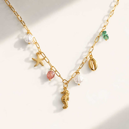 Sea Kiss goldene Halskette mit Seepferdchen, Seestern, Muschel und Perlen-Charms auf cremefarbenem Hintergrund

