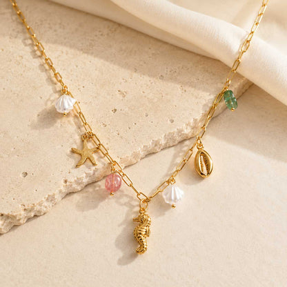 Sea Kiss goldene Halskette mit Seepferdchen, Seestern, Muschel und Perlen-Charms auf cremefarbenem Hintergrund