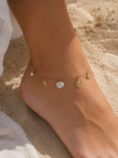 Fuß einer Frau am Strand trägt die Sea Whisper goldene Fußkette mit Seestern, Muschel und Schnecken-Medaillon – Saltyblush
