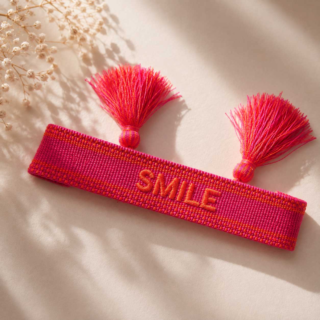 Pinkes SMILE Statement Armband mit zwei pinken Quasten aufgeklappt auf hellem Stoff, Draufsicht – Saltyblush
