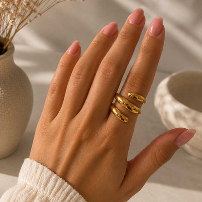 Hand einer Frau mit weißem Strickpullover trägt den Soft Curve goldenen Spiralring am Zeigefinger vor hellem Hintergrund – Saltyblush
