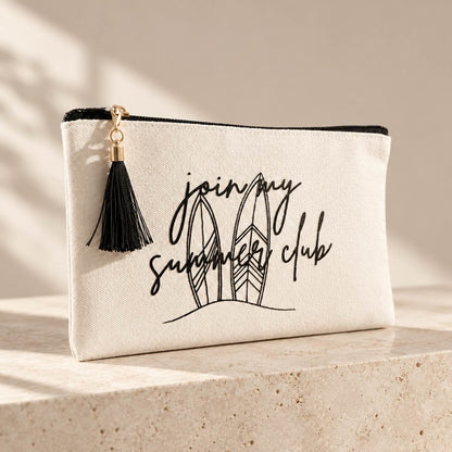 Beige summer club Kosmetiktasche mit schwarzem Reißverschluss, schwarzer Quaste und Surfbrettmotiv mit Schriftzug „join my summer club“ auf einer hellen Steinplatte.
