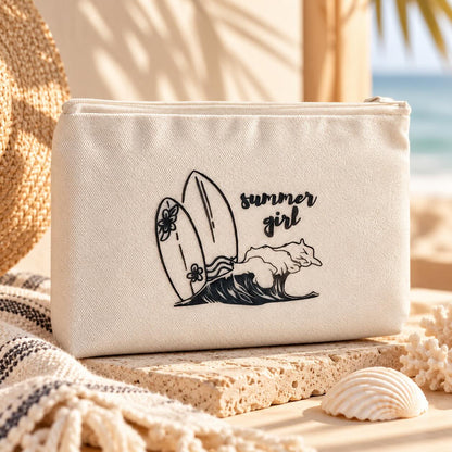 Beige summer girl Kosmetiktasche mit schwarzem Surfbrett- und Wellenmotiv auf einer Steinplatte, umgeben von Muscheln, einem Strohhut und einem gestreiften Tuch.
