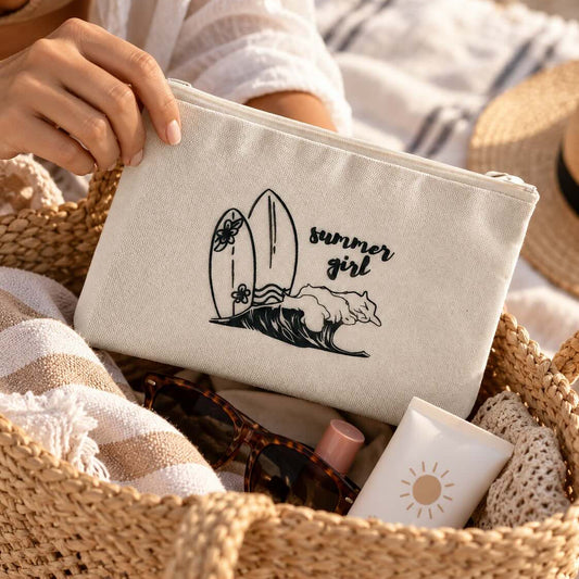 Eine Hand hält die beige summer girl Kosmetiktasche mit schwarzem Surfbrett- und Wellenmotiv über einer geflochtenen Strandtasche mit Handtuch, Sonnenbrille und Sonnencreme.
[AI]