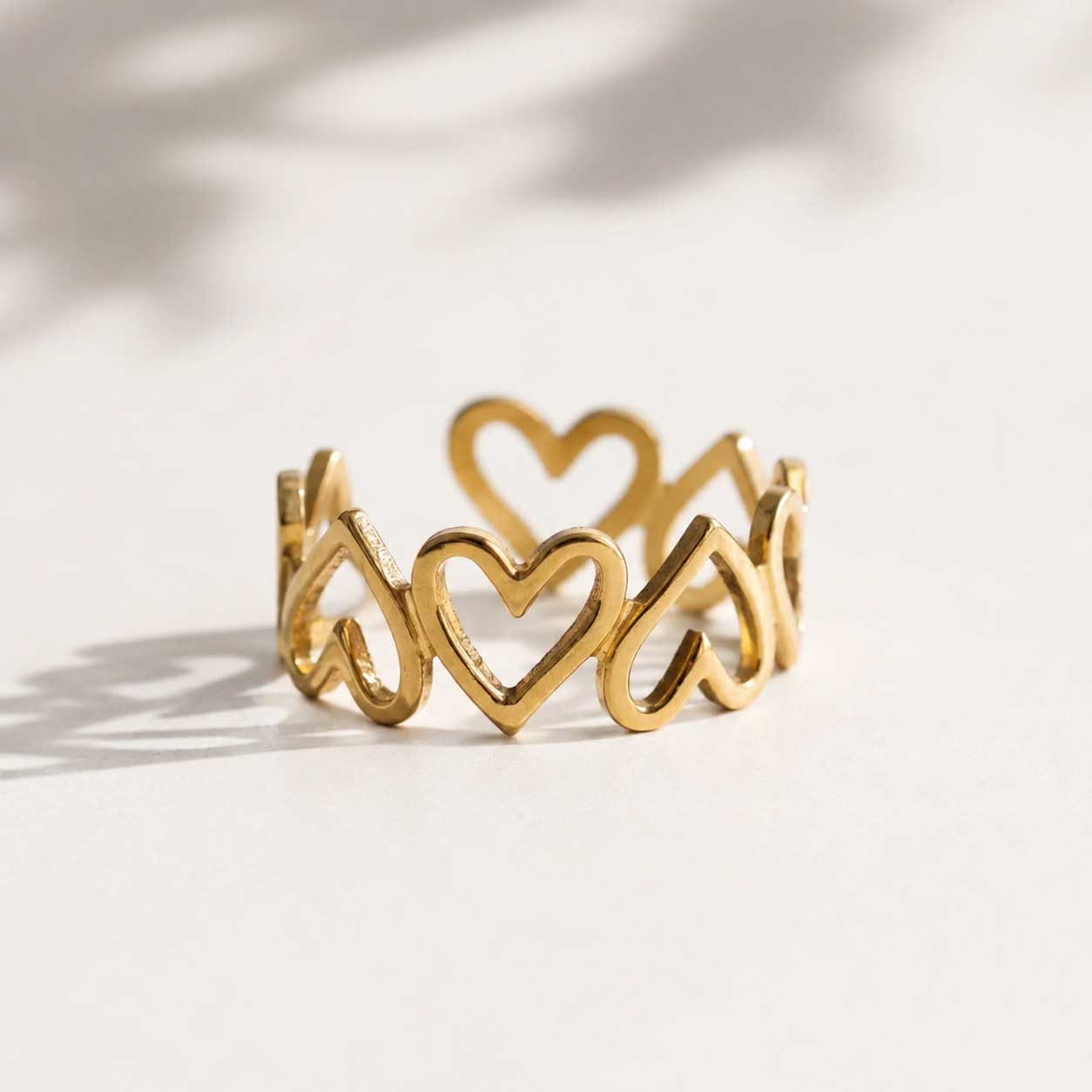 Goldener Herzring mit durchbrochenen Herz-Motiven, vergoldeter Ring auf hellem Untergrund mit Lichtschatten
