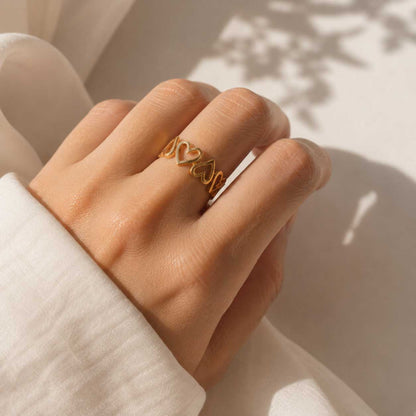 Goldener Herzring am Zeigefinger getragen, größenverstellbarer Ring mit durchbrochenen Herzen auf weißem Hintergrund
