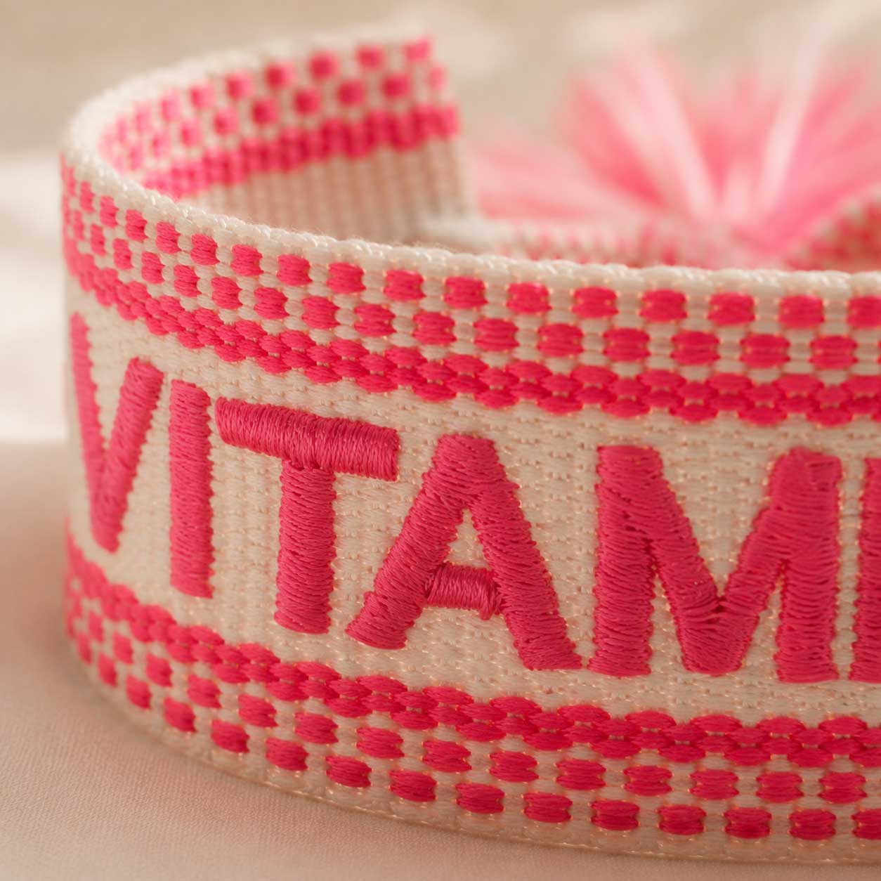 Nahaufnahme gestickter Schriftzug „Vitamin Sea" in Neonpink auf cremefarbenem Webarmband – Saltyblush
