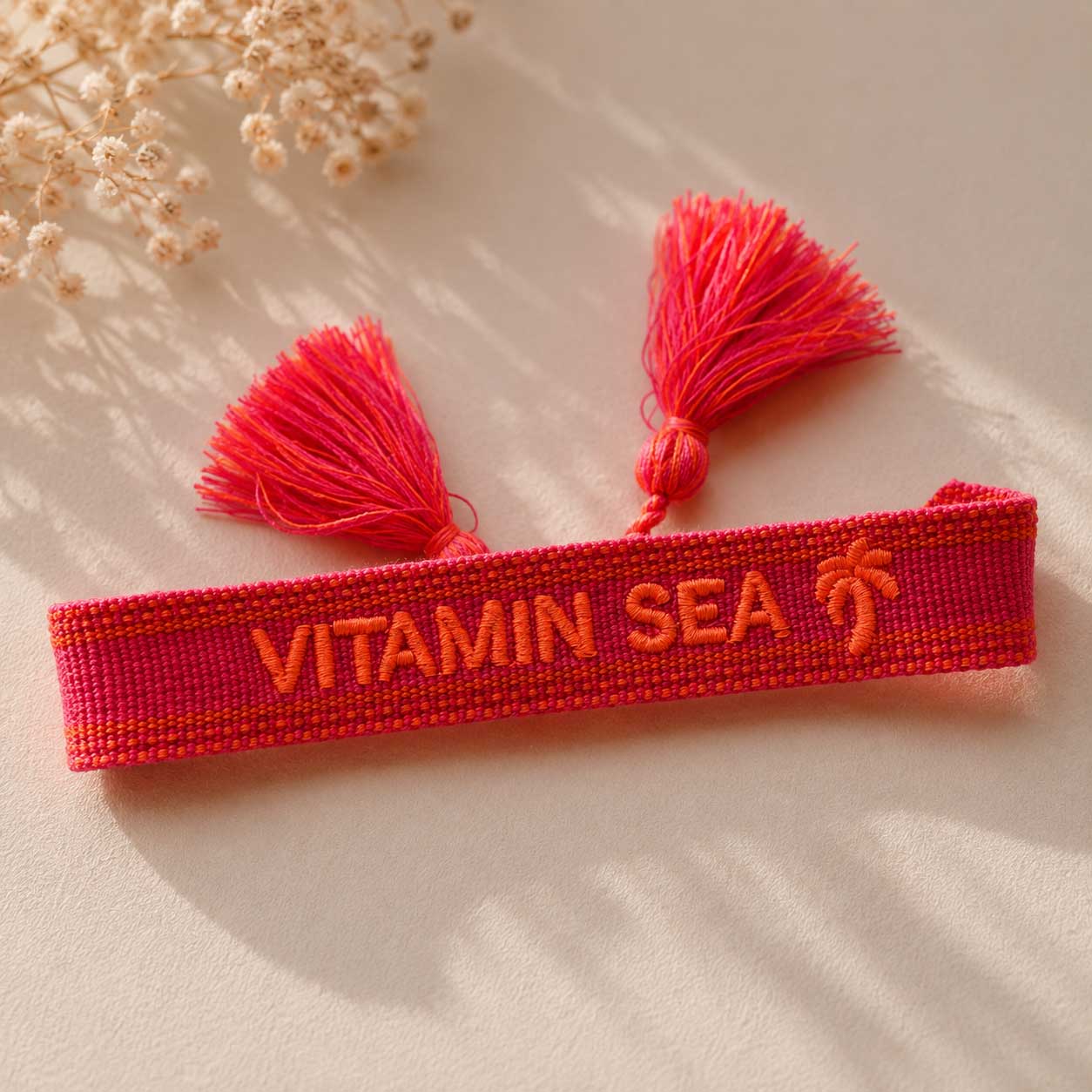 Rotes Vitamin Sea Statement Armband mit zwei pinken Quasten aufgeklappt auf hellem Stoff, Draufsicht – Saltyblush
