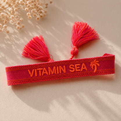 Rotes Vitamin Sea Statement Armband mit zwei pinken Quasten aufgeklappt auf hellem Stoff, Draufsicht – Saltyblush
